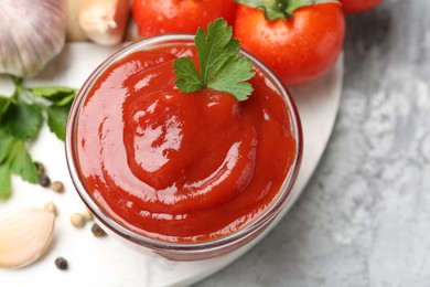 Photo of Delicious tomato ketchup and parsley in bowl on grey table, top view