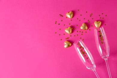 Photo of Champagne glasses and heart shaped candies in golden foil on color background, top view