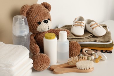 Baby clothes, toy bear and accessories on white table