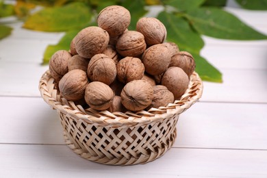 Photo of Wicker bowl of ripe walnuts on white wooden table