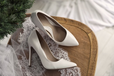Photo of Pair of white high heel shoes, veil and wreath on wooden chair indoors, above view. Dressing for wedding