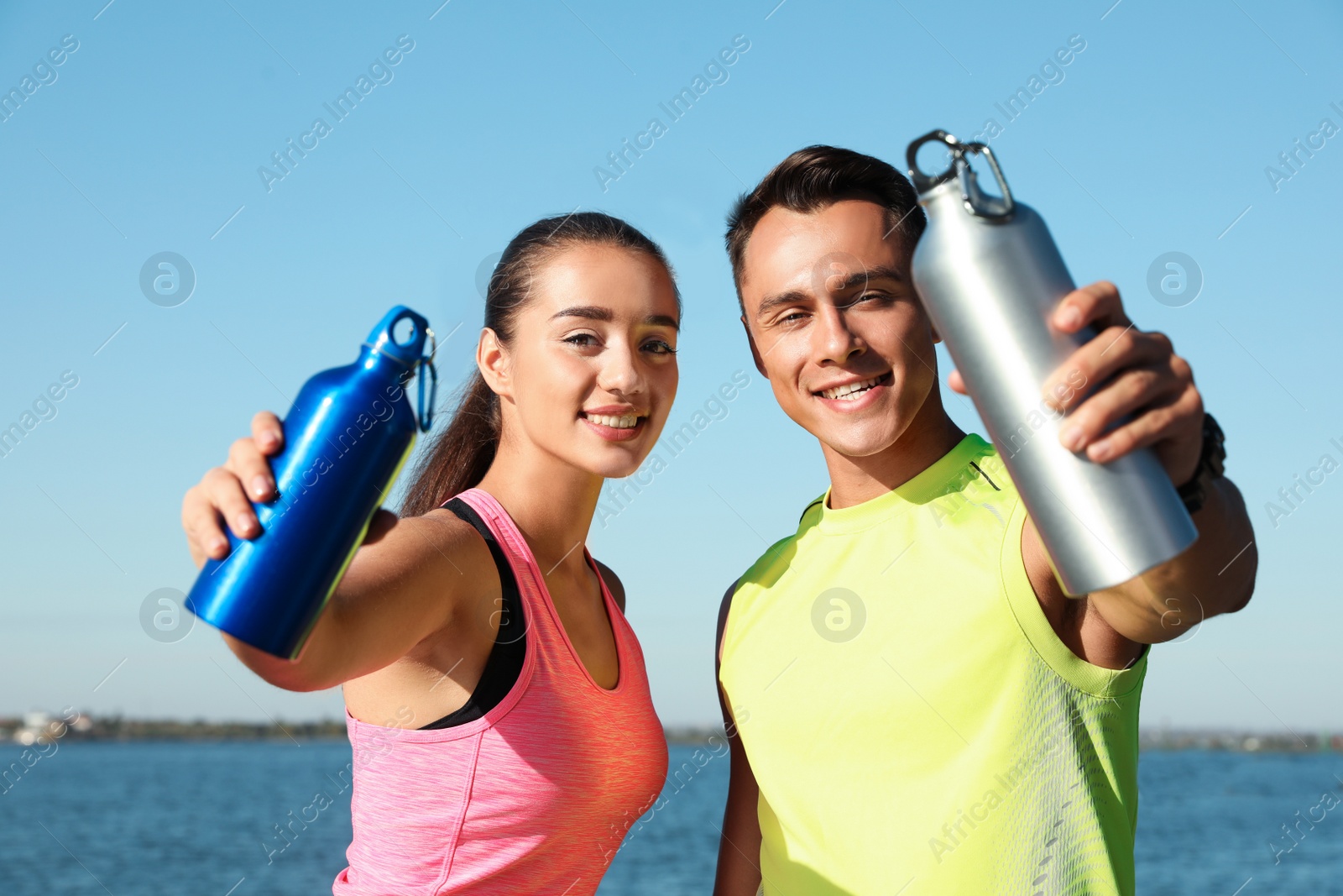 Photo of Young sporty couple with water bottles near river on sunny day