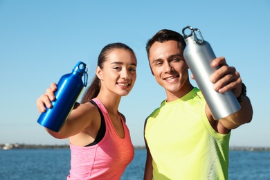 Photo of Young sporty couple with water bottles near river on sunny day