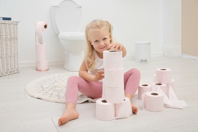 Cute little girl playing with toilet paper in bathroom