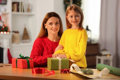 Christmas presents wrapping. Mother and her little daughter with gift boxes at table in room