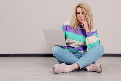 Beautiful young woman with laptop sitting on floor near grey wall. Space for text