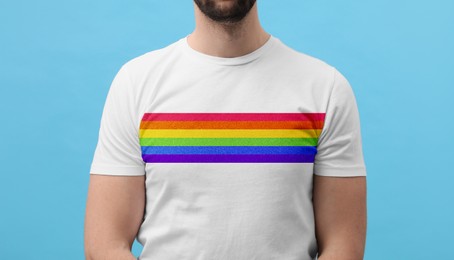 Image of Young man wearing white t-shirt with image of LGBT pride flag on turquoise background, closeup