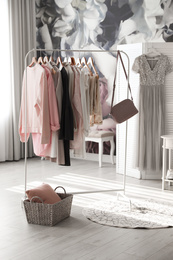 Photo of Rack with stylish women's clothes and handbag indoors. Interior design