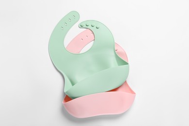 Photo of Color silicone baby bibs on white background, top view