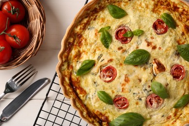 Delicious homemade cheese quiche, ingredients and cutlery on white wooden table, flat lay