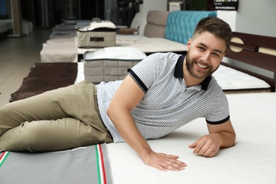 Smiling man lying on orthopedic mattress in store