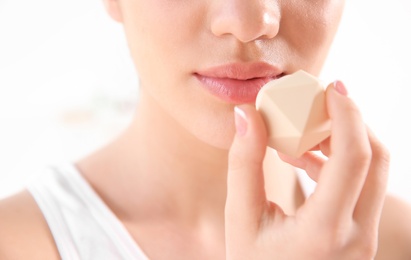 Young woman applying balm on her lips against light background, closeup