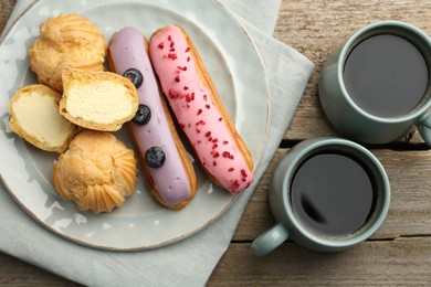 Photo of Aromatic coffee in cups, tasty eclairs and profiteroles on wooden table, top view