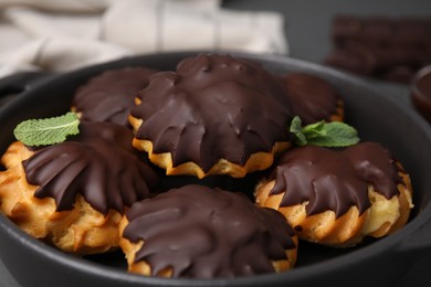 Photo of Delicious profiteroles with chocolate spread and mint in frying pan, closeup