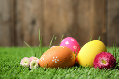 Photo of Colorful Easter eggs and daisy flowers in green grass, closeup