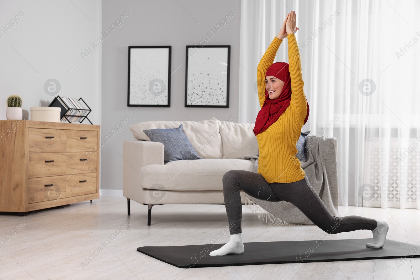 Photo of Muslim woman in hijab stretching on fitness mat at home. Space for text