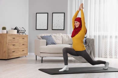 Muslim woman in hijab stretching on fitness mat at home. Space for text
