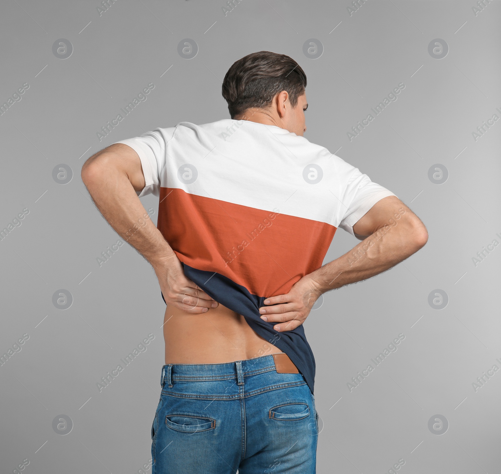 Photo of Young man suffering from back pain on grey background