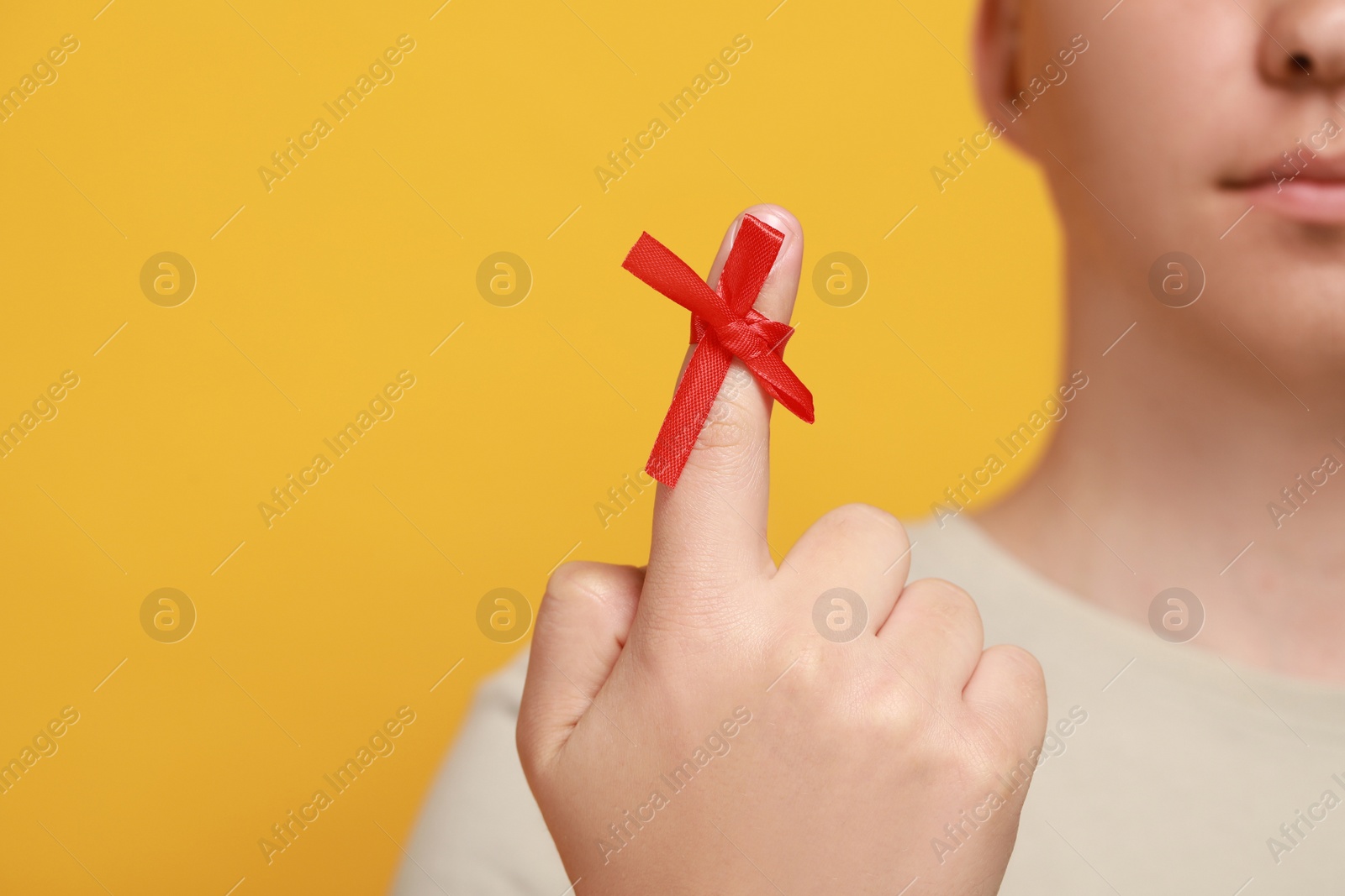 Photo of Man showing index finger with red tied bow as reminder against orange background, focus on hand. Space for text