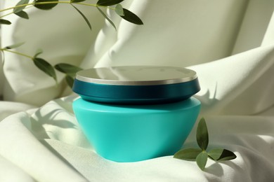 Photo of Jar of hair care cosmetic product and green leaves on light fabric