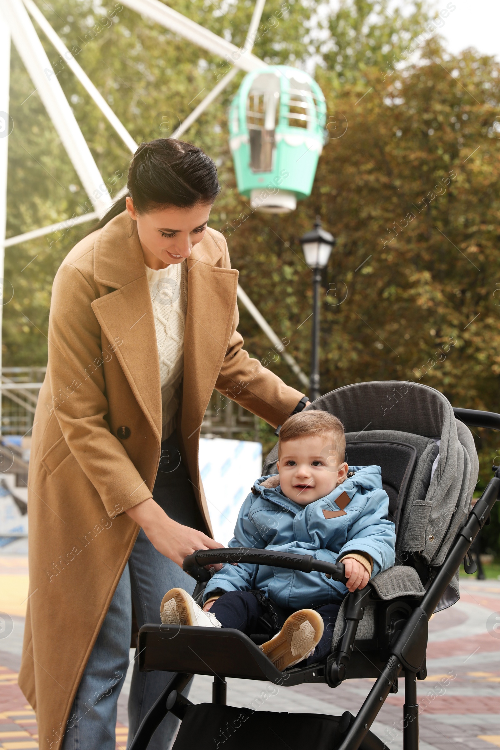 Photo of Happy mother walking with her son in stroller outdoors