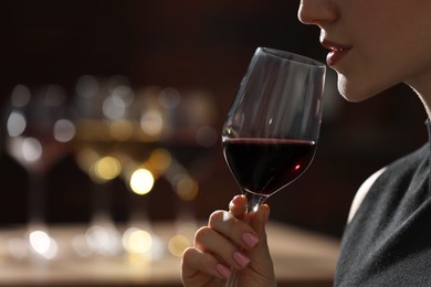 Woman with glass of red wine against blurred background, closeup. Space for text