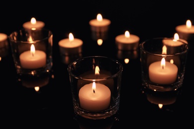 Photo of Burning candles in glass holders on dark background