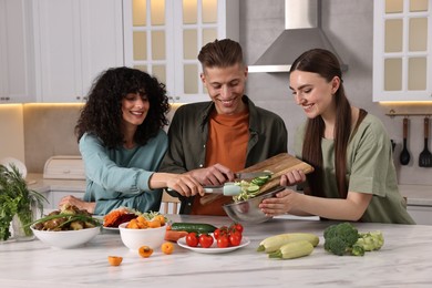 Photo of Friends cooking healthy vegetarian meal at white marble table in kitchen