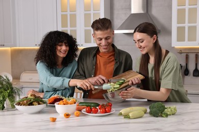 Friends cooking healthy vegetarian meal at white marble table in kitchen