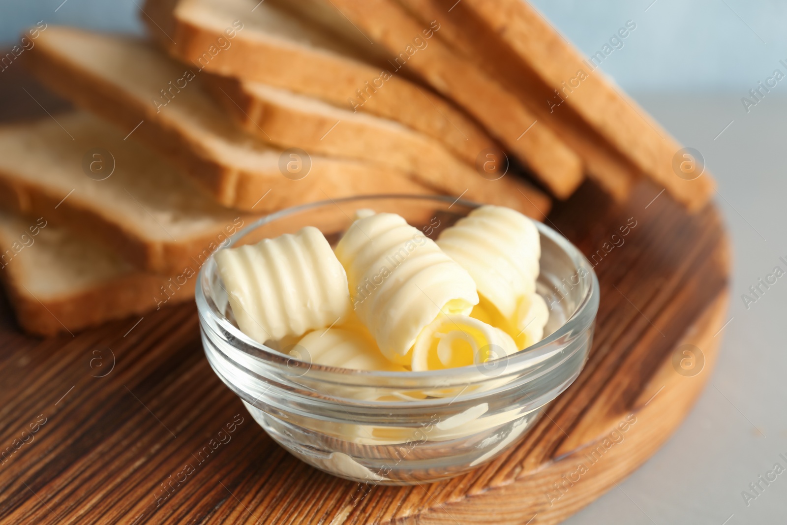 Photo of Bread with fresh butter curls on wooden board, closeup