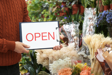 Photo of Male business owner holding OPEN sign in his flower shop, closeup