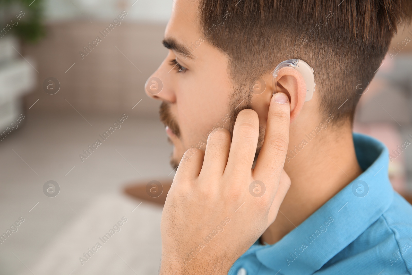 Photo of Young man adjusting hearing aid at home, closeup