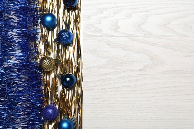 Bright tinsel and Christmas balls on white wooden background, flat lay. Space for text