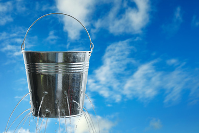 Leaky bucket with water against blue sky. Space for text