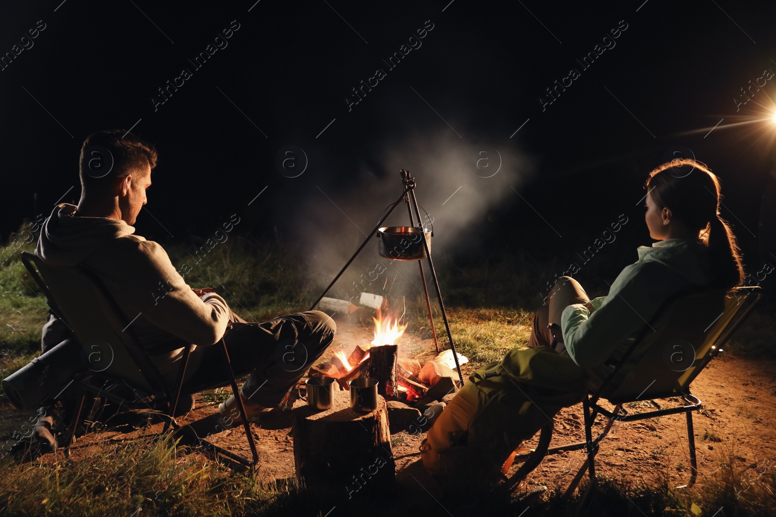 Photo of Couple near bonfire outdoors in evening. Camping season