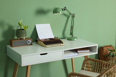 Photo of Writer's workplace with typewriter on wooden desk near pale green wall in room