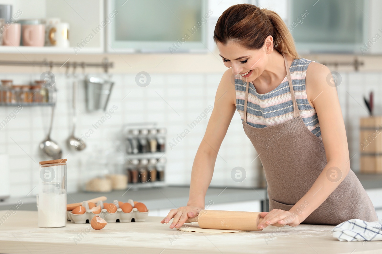 Photo of Woman rolling dough on table in kitchen