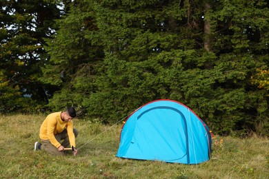 Man setting up blue camping tent near forest