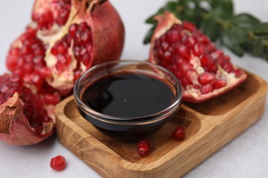 Photo of Tasty pomegranate sauce in bowl and fruits on light table, closeup