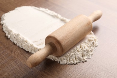 Photo of Flour and rolling pin on wooden table, closeup