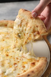 Photo of Woman taking piece of delicious cheese pizza at table, closeup