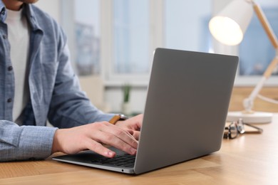 Man working on laptop at wooden desk indoors, closeup