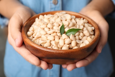 Photo of Woman holding bowl with shelled peanuts, closeup