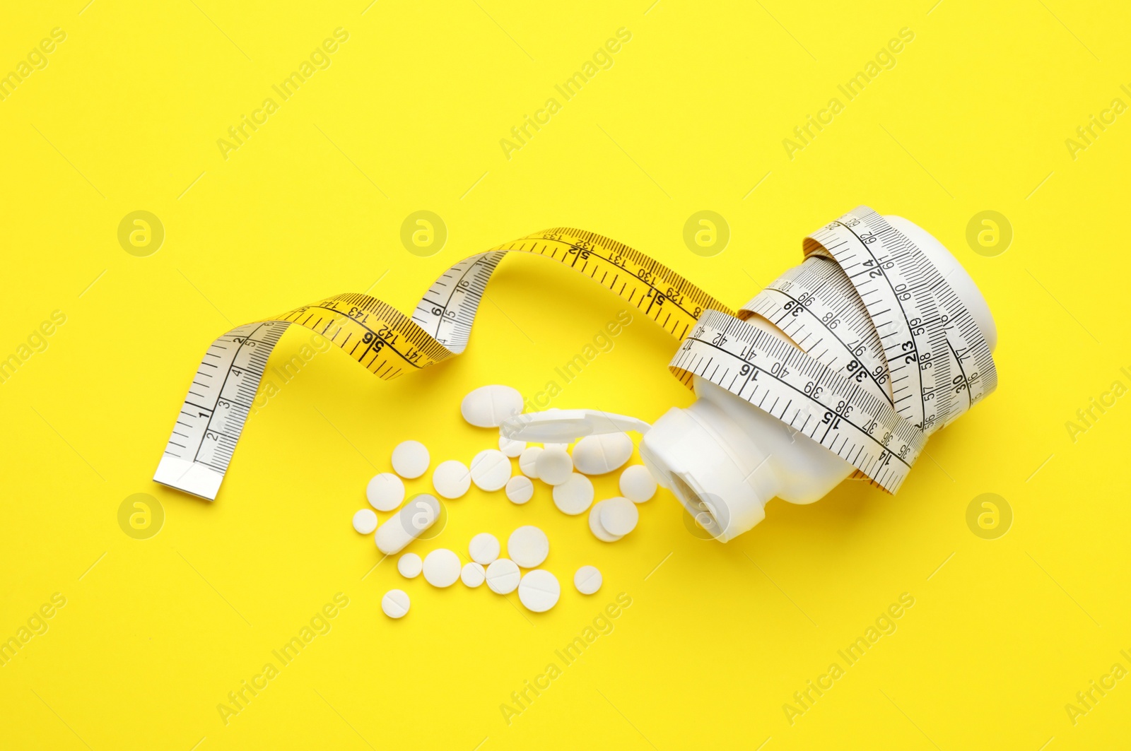 Photo of Jar of weight loss pills and measuring tape on yellow background, flat lay