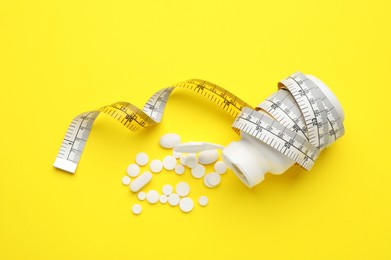 Photo of Jar of weight loss pills and measuring tape on yellow background, flat lay