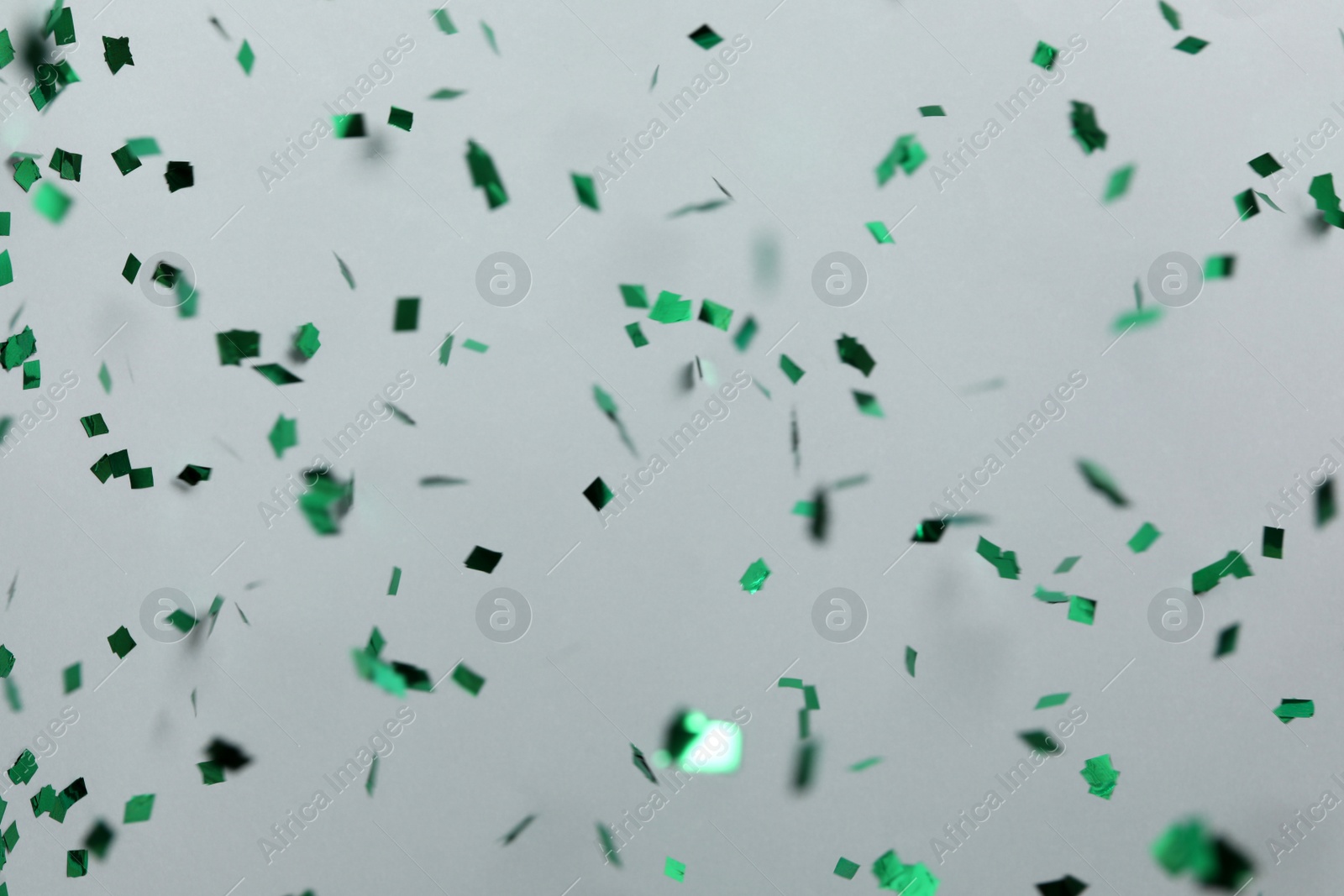 Photo of Shiny green confetti falling down on light grey background