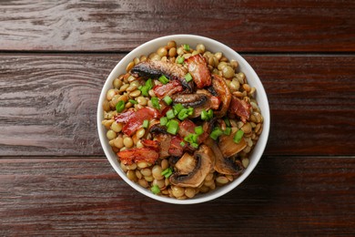 Photo of Delicious lentils with mushrooms, bacon and green onion in bowl on wooden table, top view
