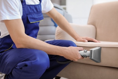 Dry cleaning worker removing dirt from sofa indoors