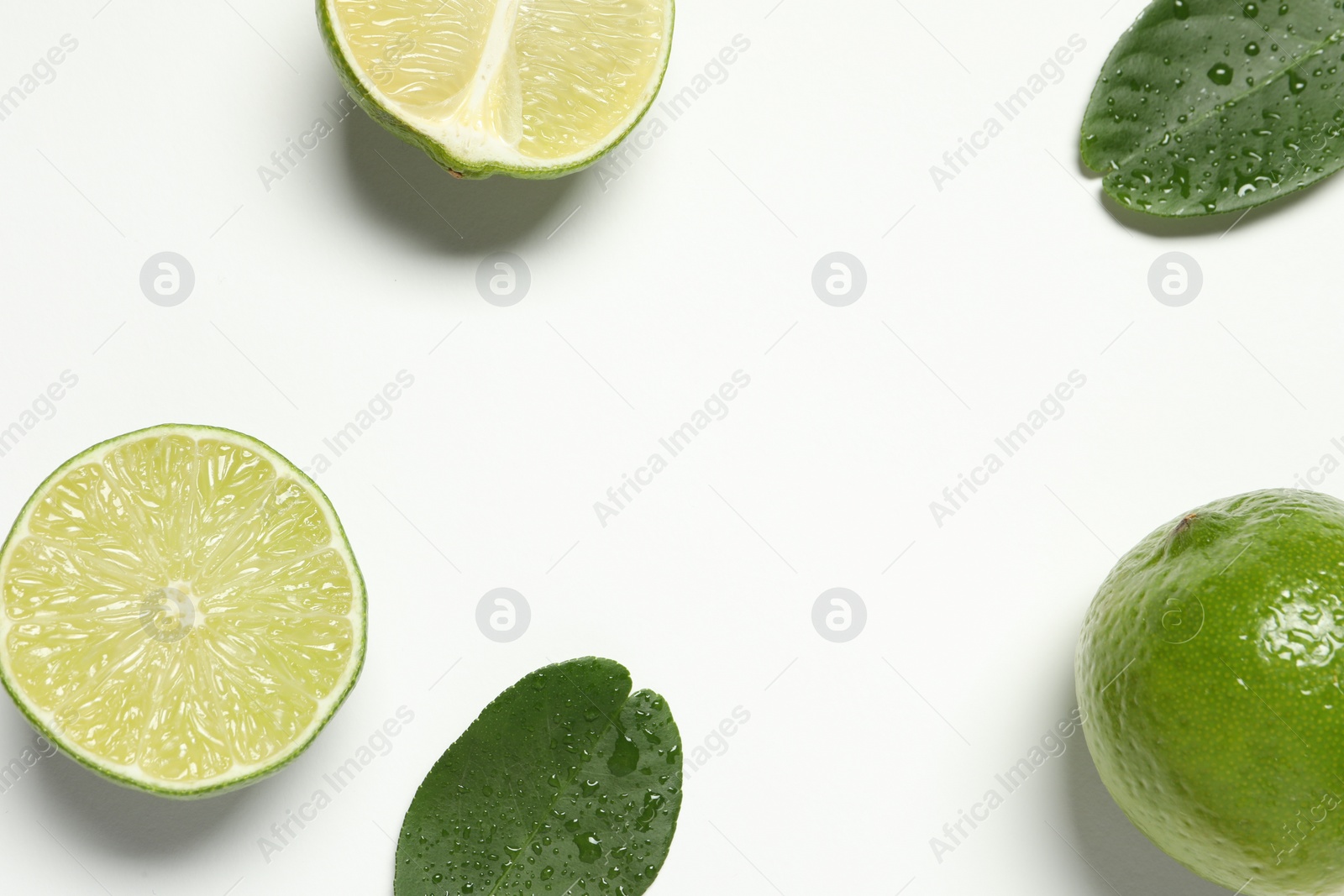 Photo of Whole and cut fresh ripe limes with green leaves on white background, flat lay