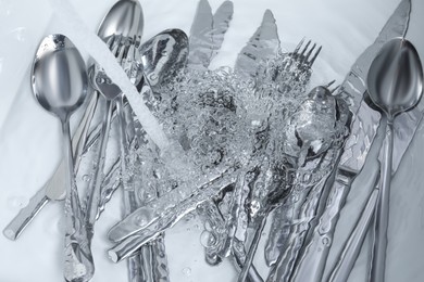 Photo of Washing silver spoons, forks and knives under stream of water in kitchen sink, top view